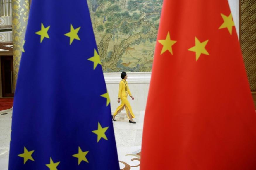 a person wearing a blue dress: FILE PHOTO: An attendant walks past EU and China flags ahead of the EU-China High-level Economic Dialogue in Beijing